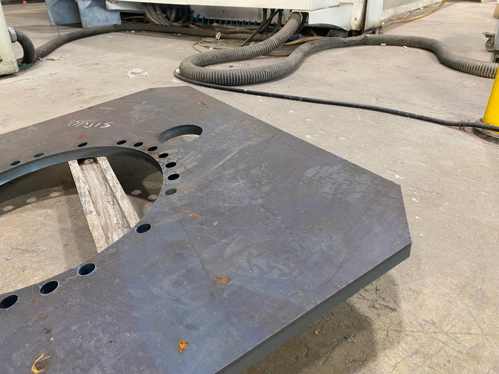 Piastra spessa in acciaio con grande foro, corona di fori e scritta SIRIO a mano, su listelli di legno in officina